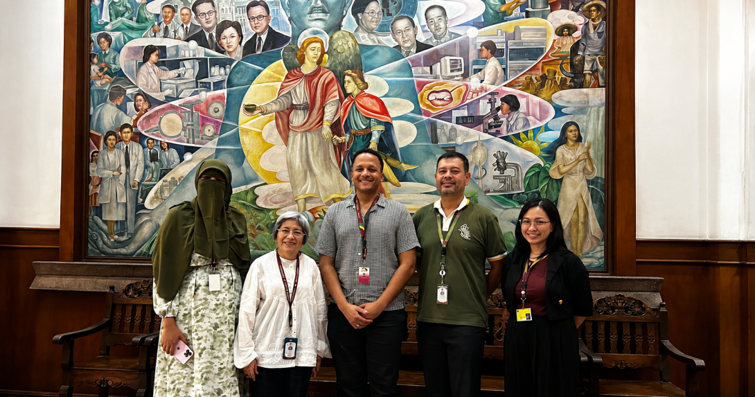 NIH representatives and visiting students pose in front of a mural at UP Manila.